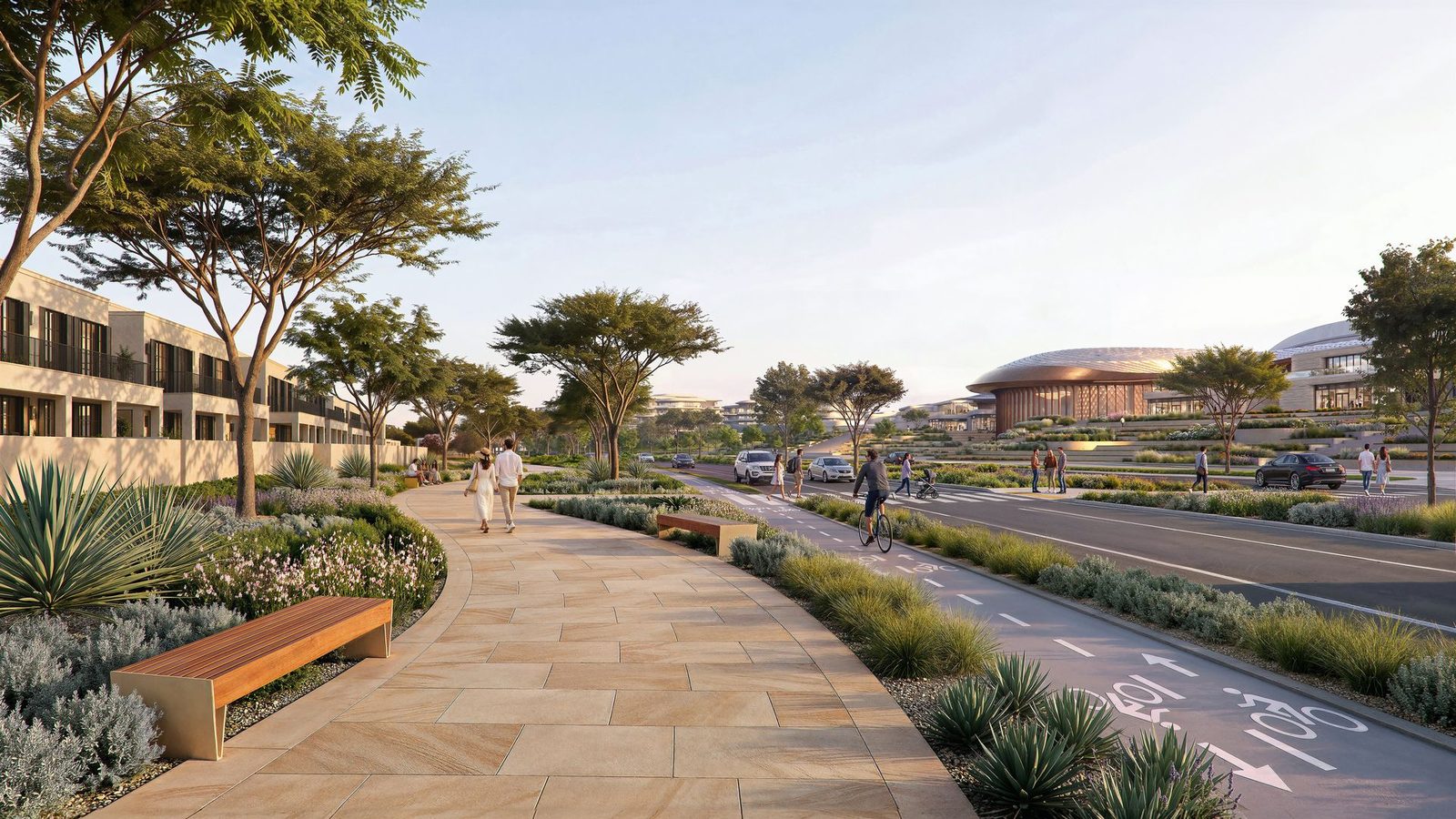 A street at Wadeem Gardens: villas on the left, a planted walking path and cycle lane, and the arena on the rise ahead