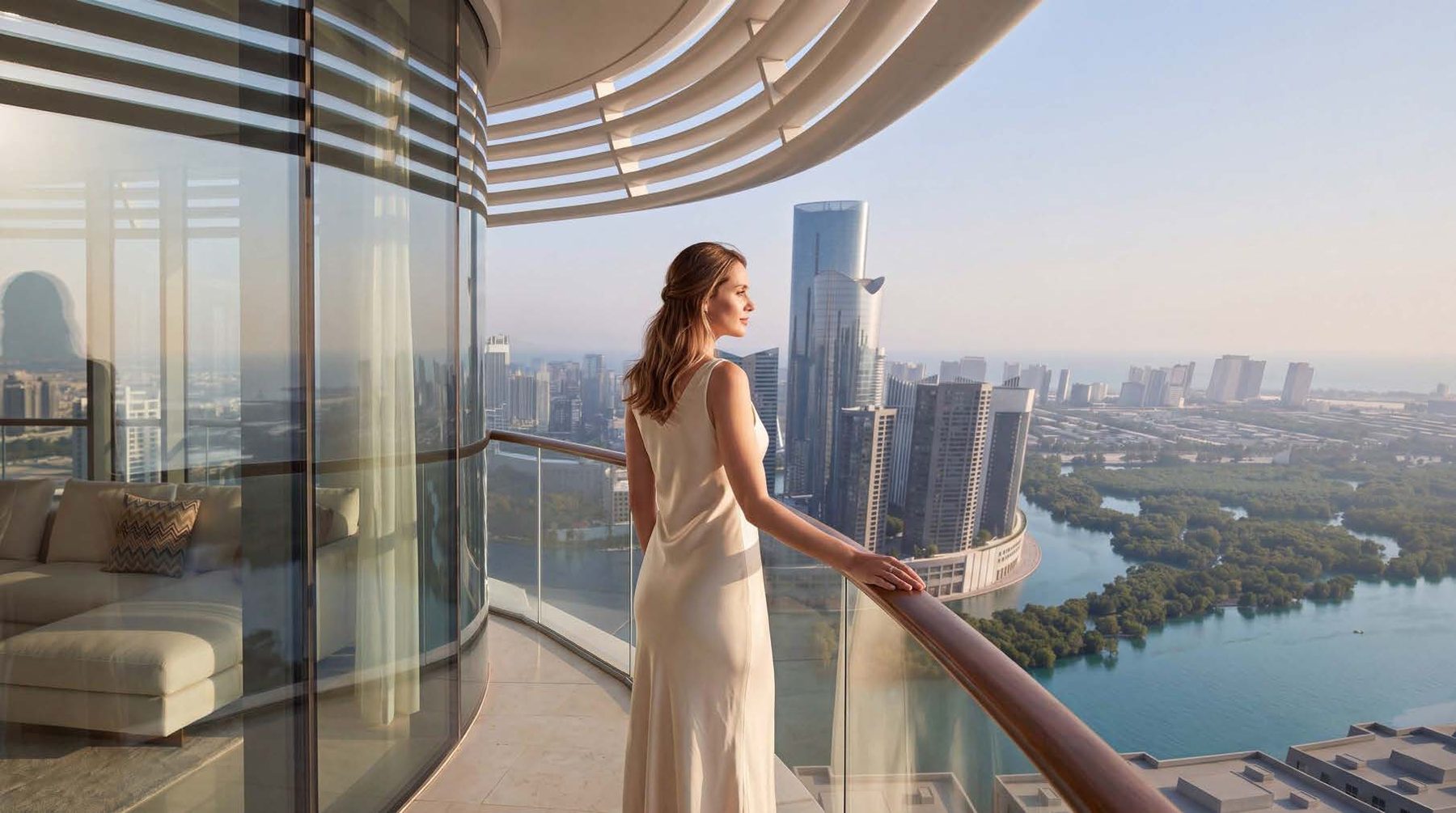 A resident on a curved balcony at Waterfront by Missoni looking across the canal and mangroves towards the Abu Dhabi skyline
